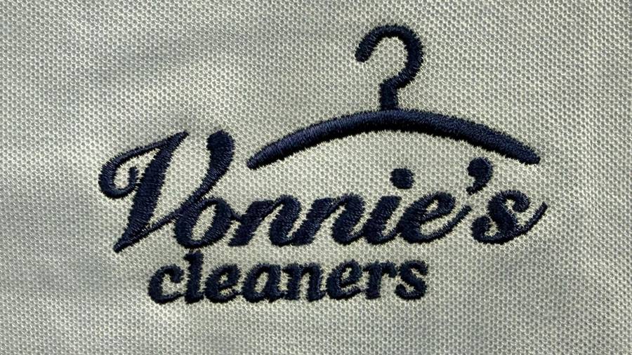 The Vonnie's cleaners script logo with a hanger, embroidered in navy thread on light fabric.